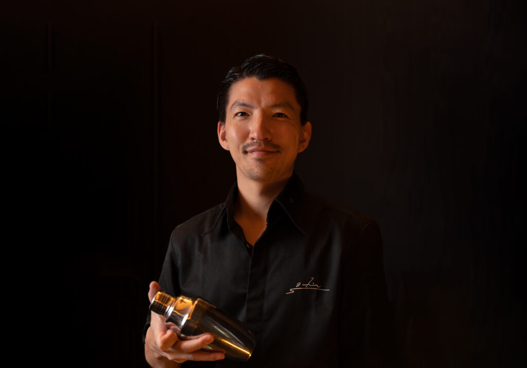 Headshot of bartender Hideyuki Saito holding a silver cocktail shaker in front of a black background