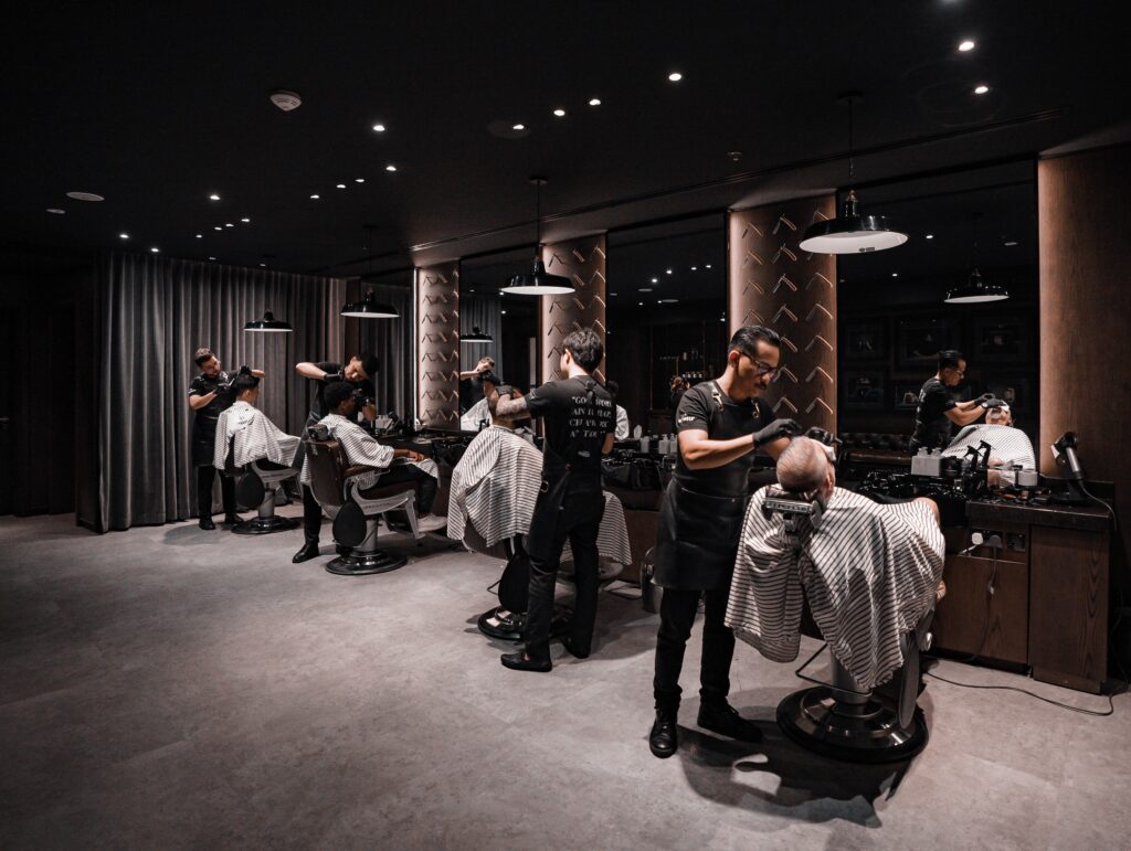 Barbers tend to clients who are seated in a barber chair and covered with a salon cape