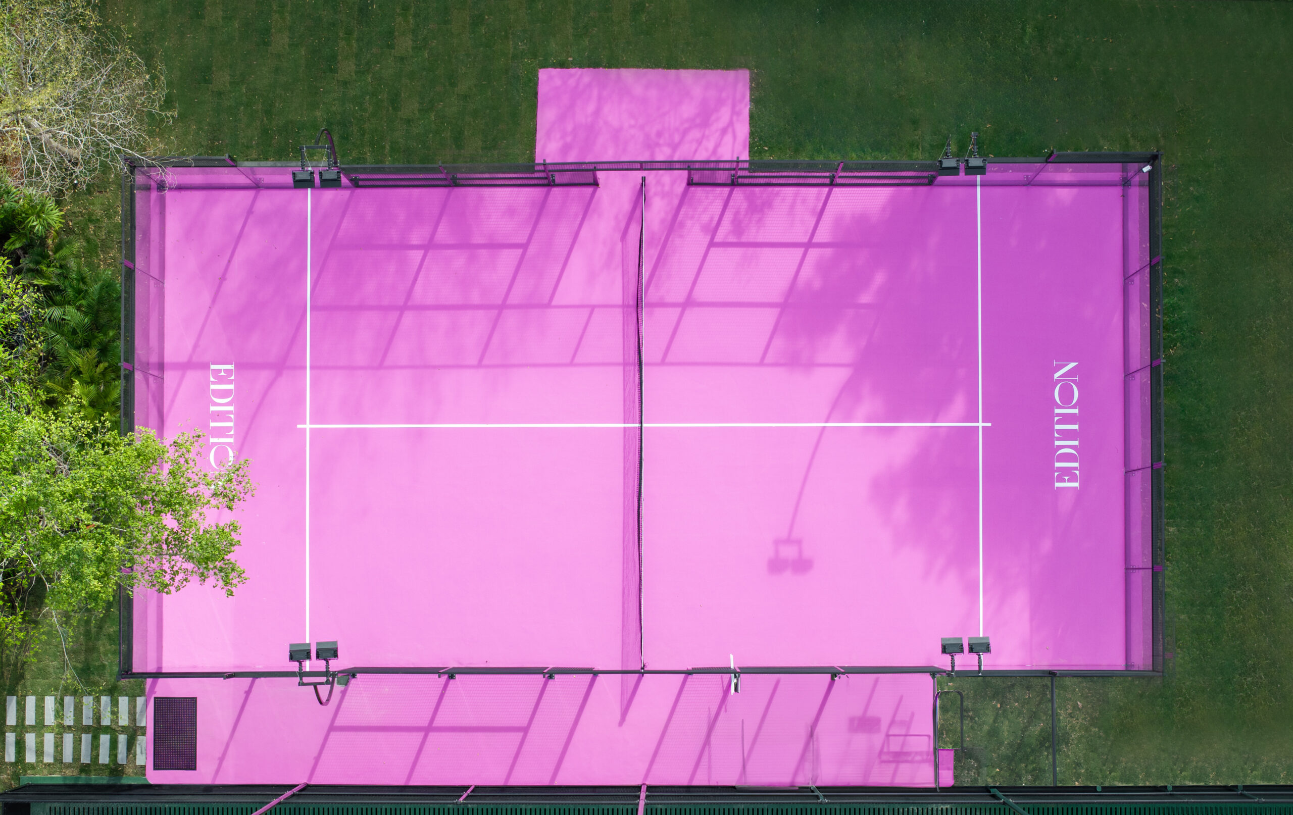 Pink padel court with EDITION branding surrounded by a manicured lawn.